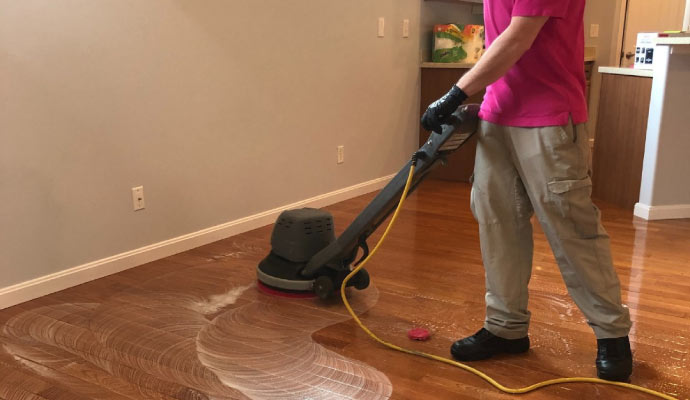 Person cleaning wooden floor with cleaning machine