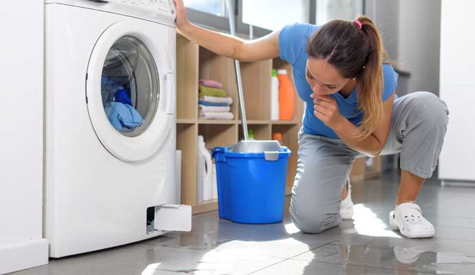 A person inspecting a washing machine that is leaking water